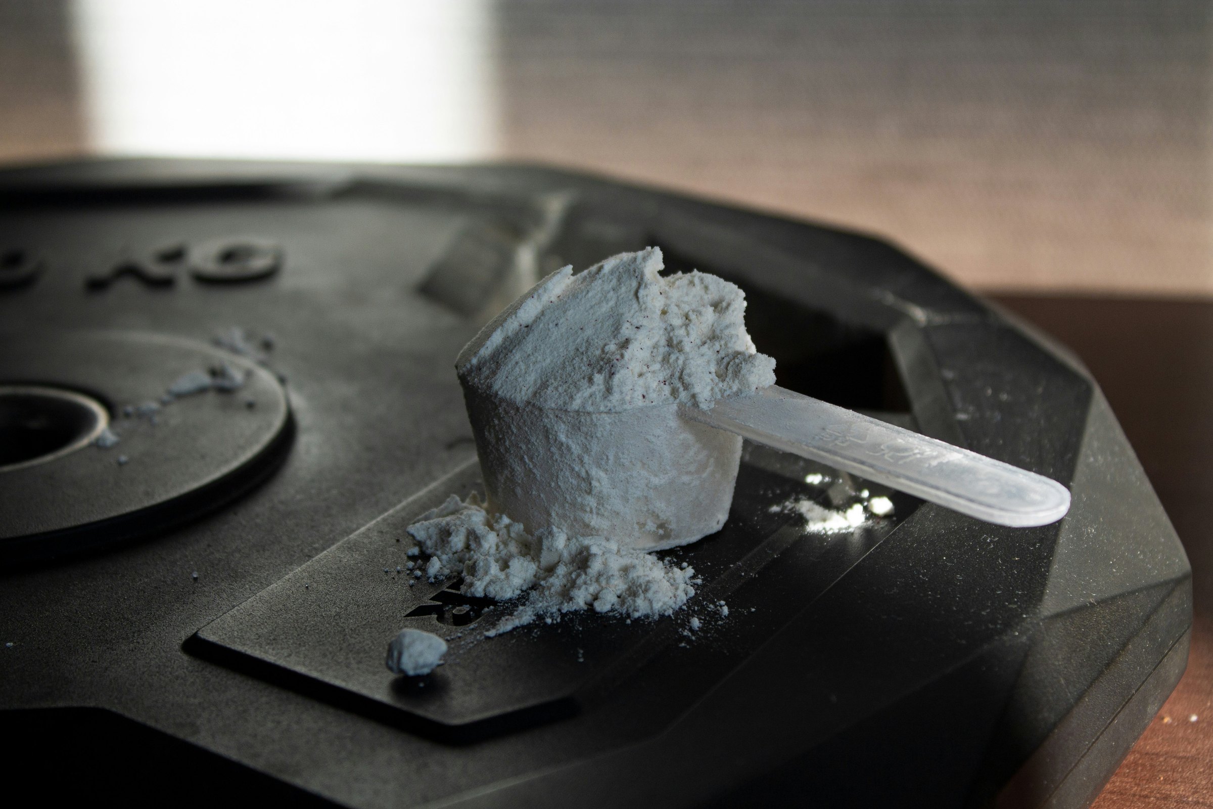 黑色槓鈴片上放著一匙滿滿的白色粉末，量匙旁散落少許粉末